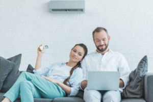 Couple sitting on the couch on their computer enjoying their ductless unit.