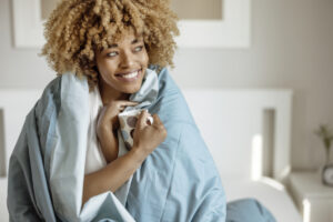 Woman snuggled under duvet with cup of coffee or tea in bed at home.