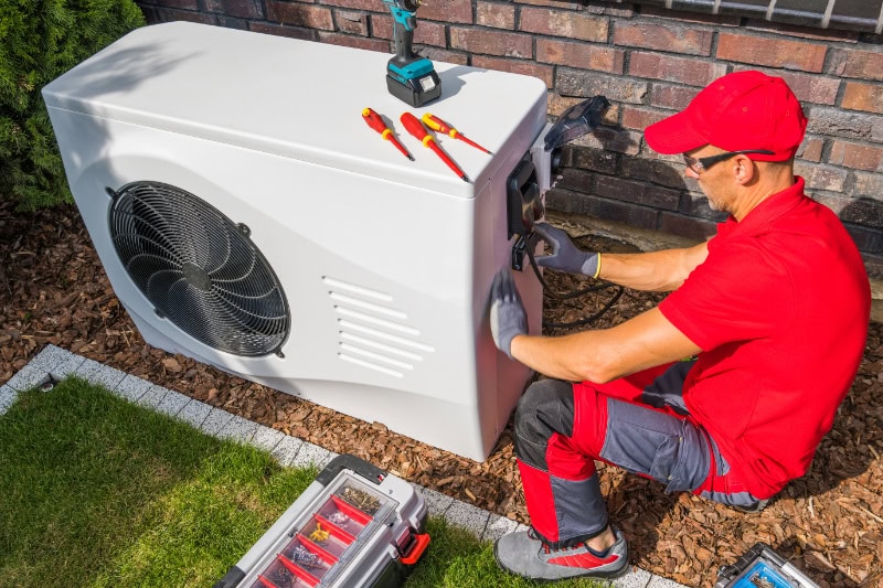 Professional HVAC Technician in Red Uniform Repairing Modern Heat Pump Unit.