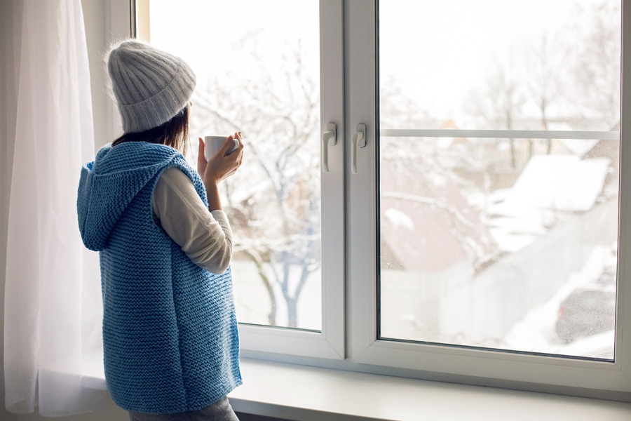 Woman inside enjoying her indoor air quality while looking out the window of her home during winter time.